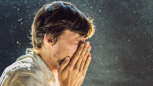Mann der in einer Staubwolke steht und sich die Hände beim Nießen vor sein Gesicht hält