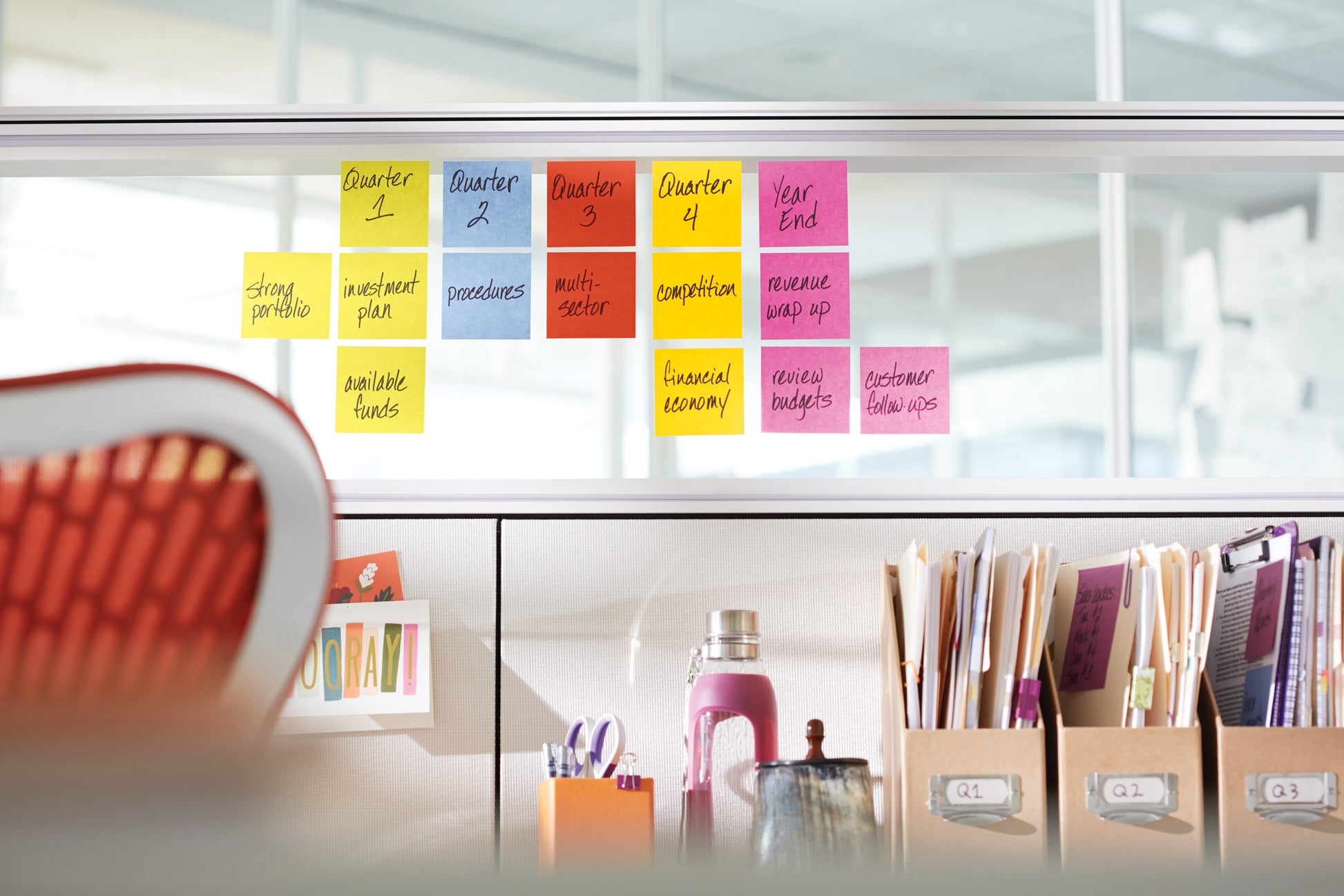 Eine Reihe von Post-it® Super Sticky Z-Notes (76 mm x 76 mm, verschiedene Farben, 20 Blöcke + 4 Gratis/Packung) von 3M Deutschland GmbH ist an einer Bürowand über einem organisierten Schreibtisch mit Büroartikeln angebracht.