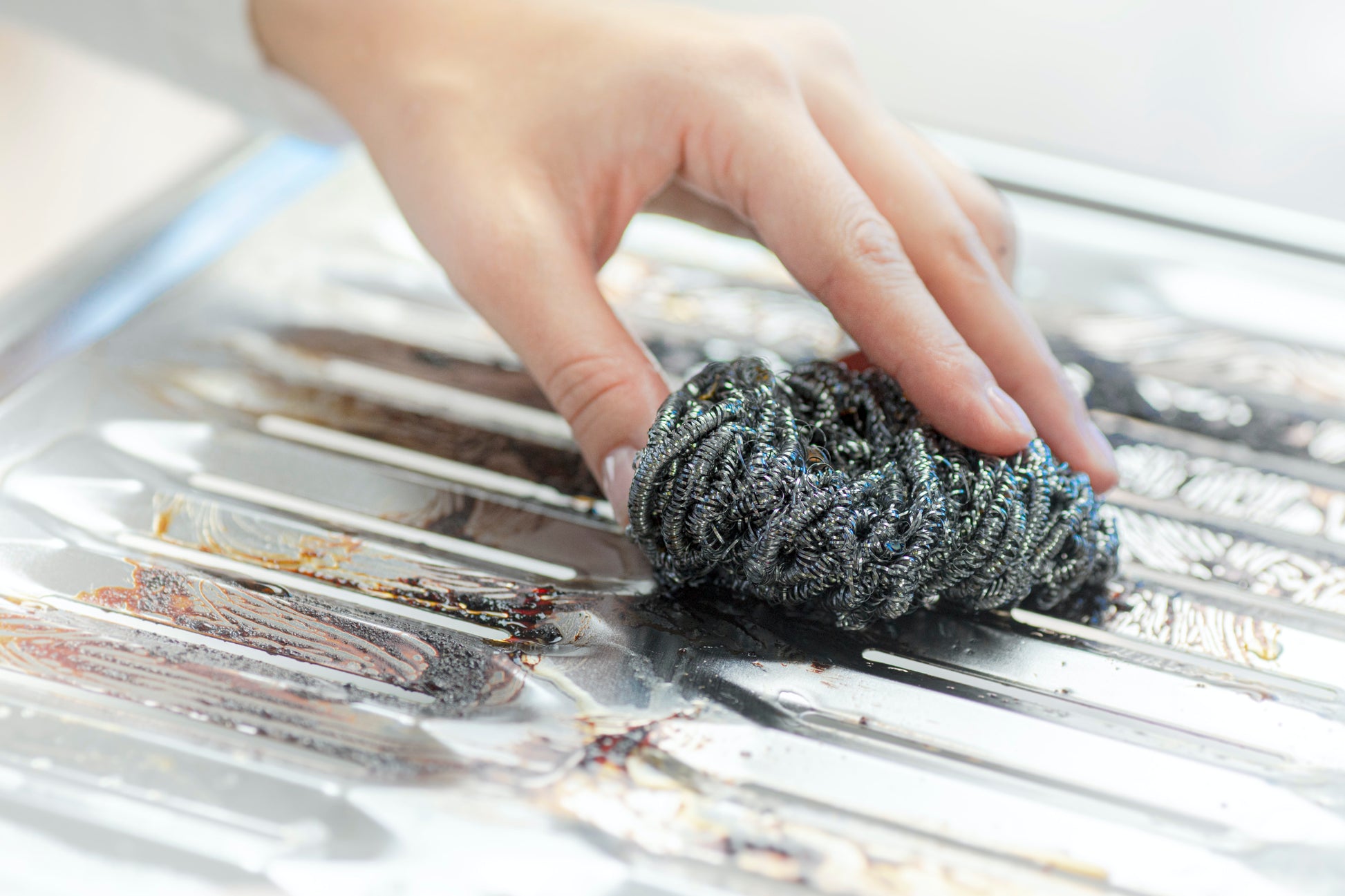 Eine Hand reinigt mit der Scotch-Brite® Edelstahl-Spirale (3 Stück/Packung) der 3M Deutschland GmbH eingebrannte Lebensmittelflecken und Fett von einer spiegelnden Metalloberfläche und schrubbt damit effektiv hartnäckigen Schmutz weg.