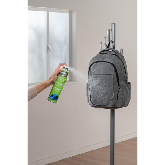 Eine Person sprüht Scotchgard™ Imprägnierspray extra stark (400ml, 1 Dose) von 3M Deutschland GmbH auf einen grauen Rucksack, der an einem Kleiderständer in der Nähe eines Fensters hängt.