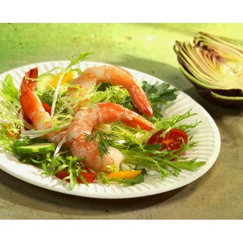 Ein PAPSTAR 100 Teller, Pappe "pure" rund, weiß extra stark der PAPSTAR GmbH hält einen Salat mit Blattgemüse, Garnelen, Gurken, gelber Paprika, Kirschtomaten und Dill. Im Hintergrund liegt ein aufgeschnittener Rotkohlkopf auf einer grünen Fläche.