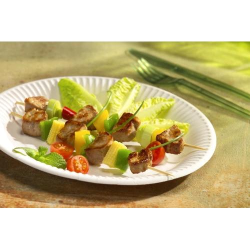 Ein PAPSTAR Pappteller rund „pure“ Ø 26 cm von PAPSTAR GmbH hält Spieße mit gegrilltem Fleisch, gelbem und grünem Gemüse sowie Tomaten und frischen Salatblättern; Im Hintergrund liegen Plastikgabel und Messer.