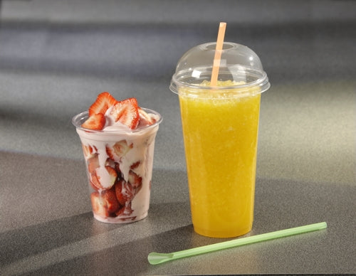 Ein mit Erdbeeren und Joghurt gefüllter Starpak 50 Trinkbecher "Hurricane" PET-Glasklar steht neben einem hohen To-Go-Becher mit orangefarbenem Slush, der mit einem Kuppeldeckel und Strohhalm versehen ist. Auf der grauen Arbeitsplatte daneben liegt ein grüner Rührstab.