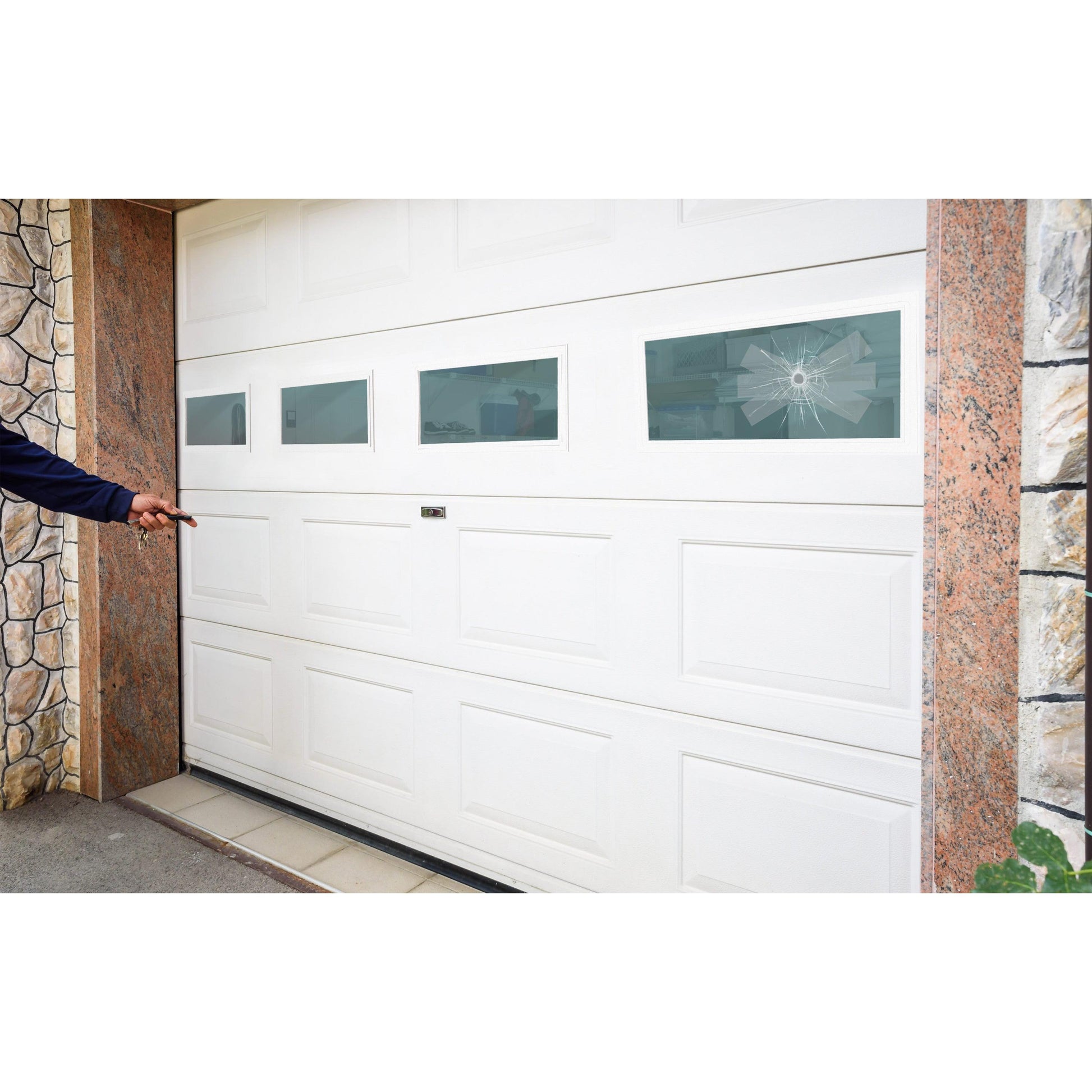 Eine Person zeigt auf ein weißes Garagentor mit vier rechteckigen Fenstern, von denen eines in einem Spinnennetzmuster zerbrochen ist - ideal für die Reparatur mit 3M Deutschland GmbH Scotch® Extremium™ INVISIBLE Hochleistungs-Klebeband (20 m x 48 mm). Stein und Fliesen grenzen die Garage ein.