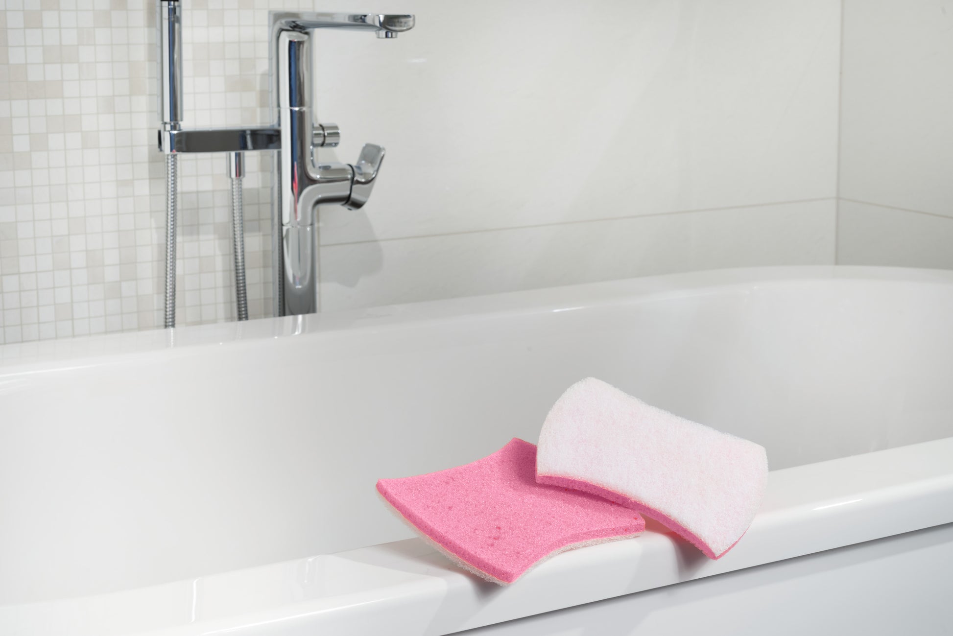 Ein Scotch-Brite® Bath XXL Reinigungsschwamm (1 Stück, 3M Deutschland GmbH) liegt am Rand einer weißen Badewanne bei einem Chrom-Wasserhahn und Fliesen.