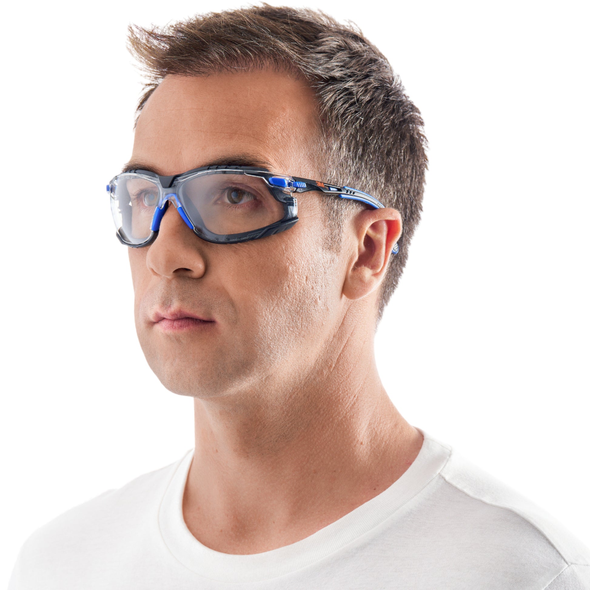 Ein Mann mit kurzen braunen Haaren, der die 3M™ Solus™ Schutzbrille 1000 der 3M Deutschland GmbH mit Scotchgard™ Antibeschlag-Beschichtung und klarer Scheibe trägt, blickt in einem schlichten weißen T-Shirt vor weißem Hintergrund leicht zur Seite.