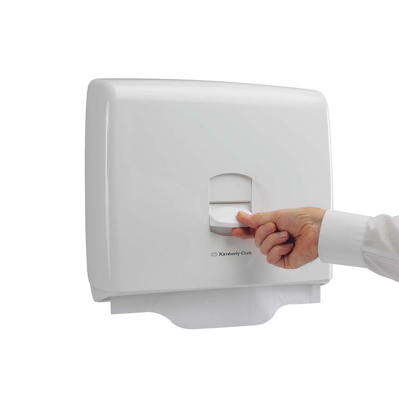 Eine Hand zieht ein Papierblatt aus dem weißen Aquarius™ Toilettensitzauflagenspender der Kimberly-Clark GmbH, der für Hygiene in öffentlichen Toiletten wirbt, vor einem schlichten weißen Hintergrund.