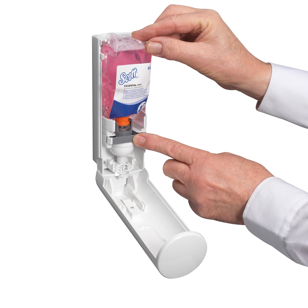 Eine Person führt eine Scott® ESSENTIAL™ Schaumseife Kassette (Rosa, 200ml) von Kimberly-Clark GmbH in einen Wandspender ein und drückt auf den orangefarbenen Teil, während der geöffnete Deckel das Innere und den rosa Schaumseifenbehälter zeigt.