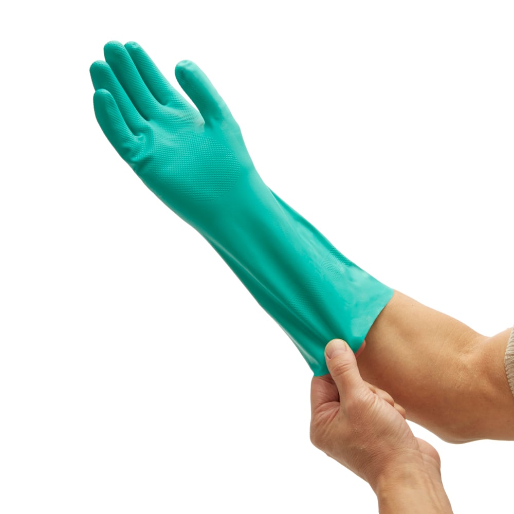 Eine Person zieht einen grünen Kimberly-Clark GmbH KleenGuard® G80 Chemikalienschutzhandschuh (33 cm, handspezifische Paare) an, der ihre Hand und ihren Unterarm bedeckt, vor einem einfarbig weißen Hintergrund.