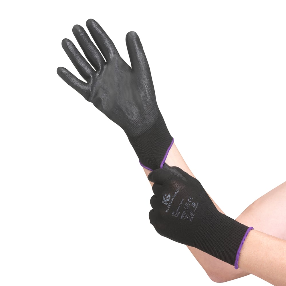 Eine Person zieht schwarze KleenGuard® G40 Polyurethanbeschichtete Handschuhe der Kimberly-Clark GmbH an, die sich durch eine strukturierte Oberfläche, eine Abdeckung der Handgelenke und einen aufgedruckten Text auf der Rückseite auszeichnen. Nur ihre Unterarme und Hände sind sichtbar.