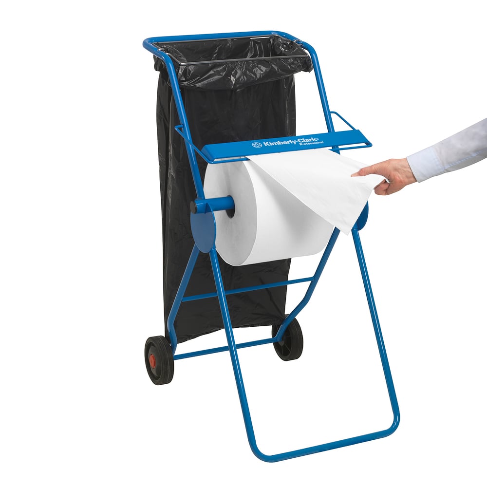 Ein blauer Metallspender hält ein WypAll® L10 Papierwischtuch für Oberflächen - Großrolle (38 x 23,5 cm) der Kimberly-Clark GmbH und einen schwarzen Müllsack; eine Person zieht ein Blatt für die Oberflächenreinigung heraus.