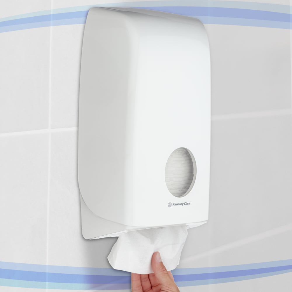 Eine Hand zieht Toilettenpapier aus einem weißen Aquarius™ Toilettenpapierspender von Kimberly-Clark GmbH, der zur hygienischen Aufbewahrung in einem gefliesten Badezimmer an der Wand montiert ist.