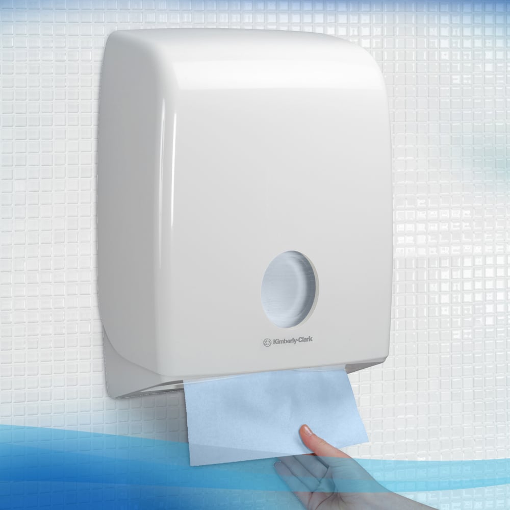 Eine Hand zieht ein blaues Scott® Control™ Falthandtücher Interfold aus einem weißen Spender der Kimberly-Clark GmbH, wobei die Schachtel 15 Packungen mit je 240 Blatt enthält, vor einem gekachelten Hintergrund.