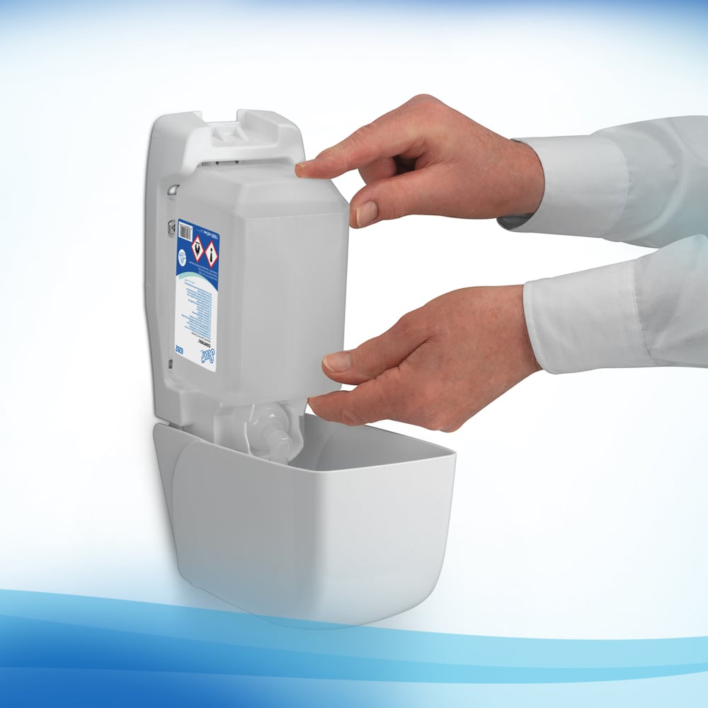 Eine Person befüllt einen wandmontierten Spender mit einer Scott® CONTROL Handdesinfektionsschaum auf Alkoholbasis 1L Kassette von Kimberly-Clark GmbH und zeigt dabei das Warnschild. Ihre Hände sind sichtbar und sie trägt ein weißes langärmeliges Hemd.