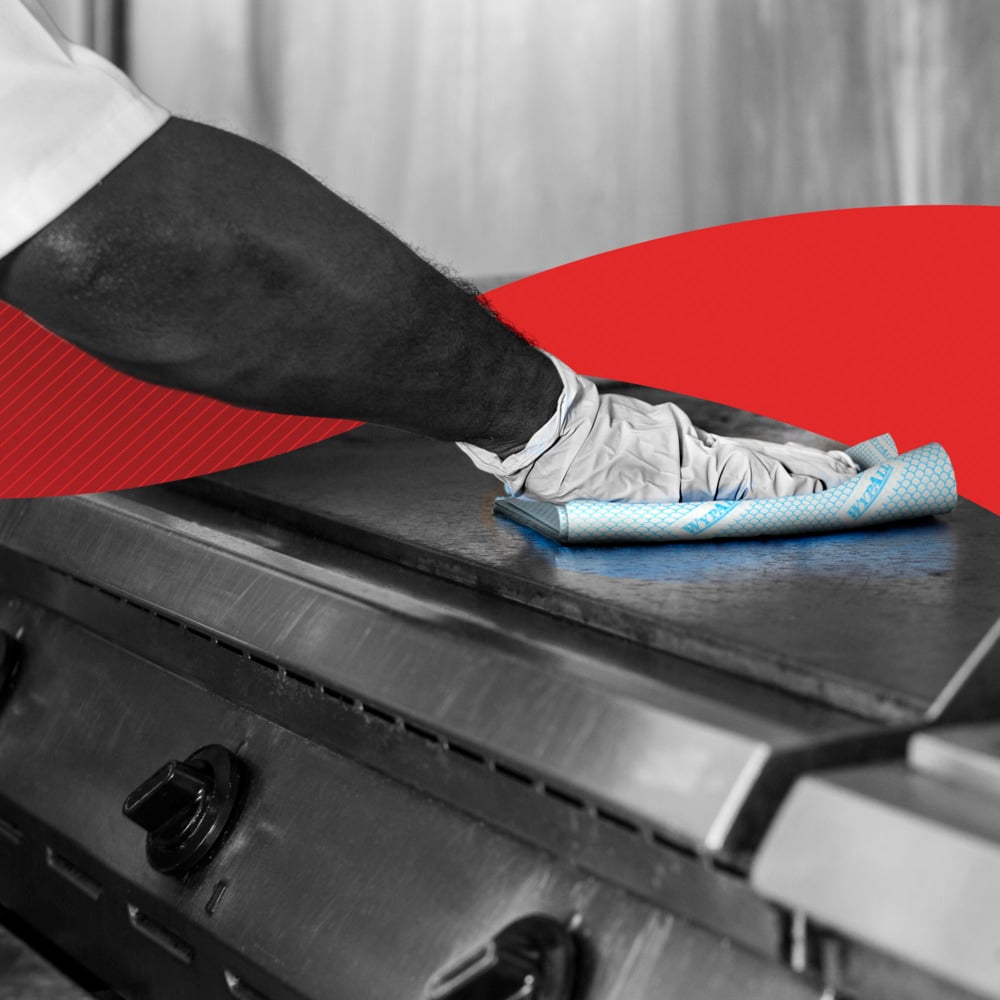 Eine Person mit Handschuhen reinigt eine Herdplatte aus Edelstahl mit einem WypAll® X80 Critical Clean - Interfold (41 x 33 cm) Reinigungstuch der Kimberly-Clark GmbH. Eine rote Grafik unterstreicht die Verwendung in industriellen Reinigungsumgebungen.