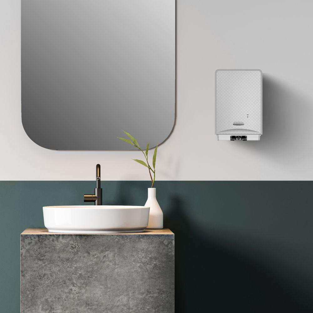 Ein modernes Badezimmer verfügt über einen runden Spiegel, ein weißes Gefäßwaschbecken, einen schwarzen Wasserhahn und den Scott® Control™ Schaum-Handreiniger (4 Kartuschen) von Kimberly-Clark GmbH für optimale Handhygiene. Neben dem Waschbecken steht eine Vase mit grünen Blättern, rechts daneben befindet sich ein Warmwasserbereiter.