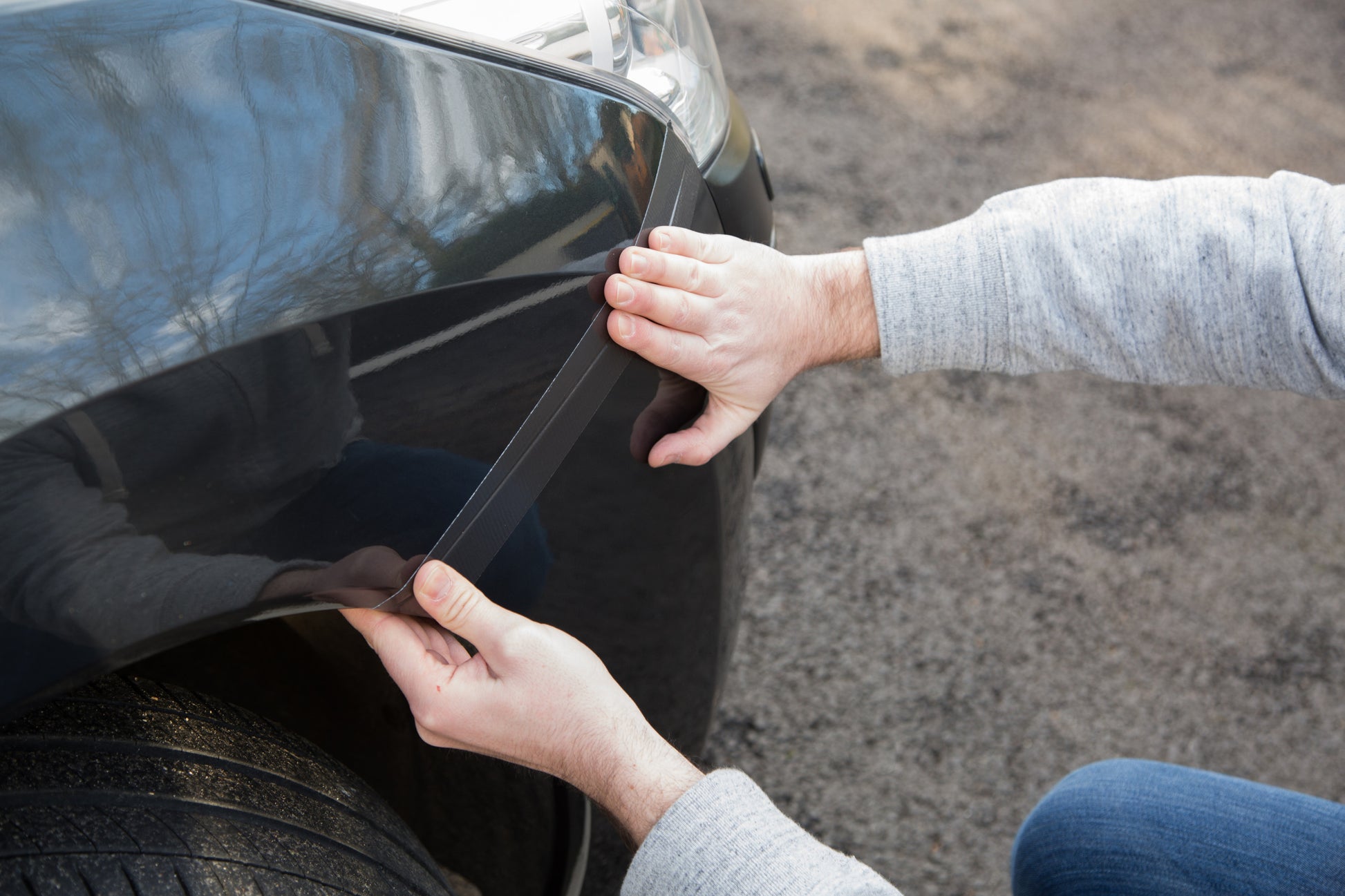 Eine Person bringt das Scotch® Extremium™ No Residue Hochleistungs-Gewebeklebeband (18,2 m x 48 mm) von 3M an der vorderen Kotflügelkante des Autos an und drückt es auf den Lack, um die Oberfläche zu schützen, ohne Rückstände zu hinterlassen.