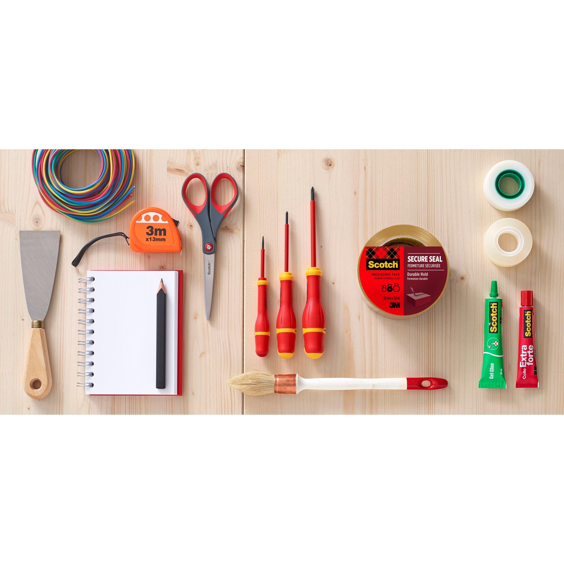 Eine flache Lage zeigt verschiedene Werkzeuge und Hilfsmittel auf Holz, darunter Scotch® Verpackungsklebeband (50 mm x 66 m) von 3M Deutschland GmbH, Schere, Schraubenzieher, Pinsel, Kleber, Spachtel, farbiger Draht, Notizbuch mit Bleistift und andere Bänder.