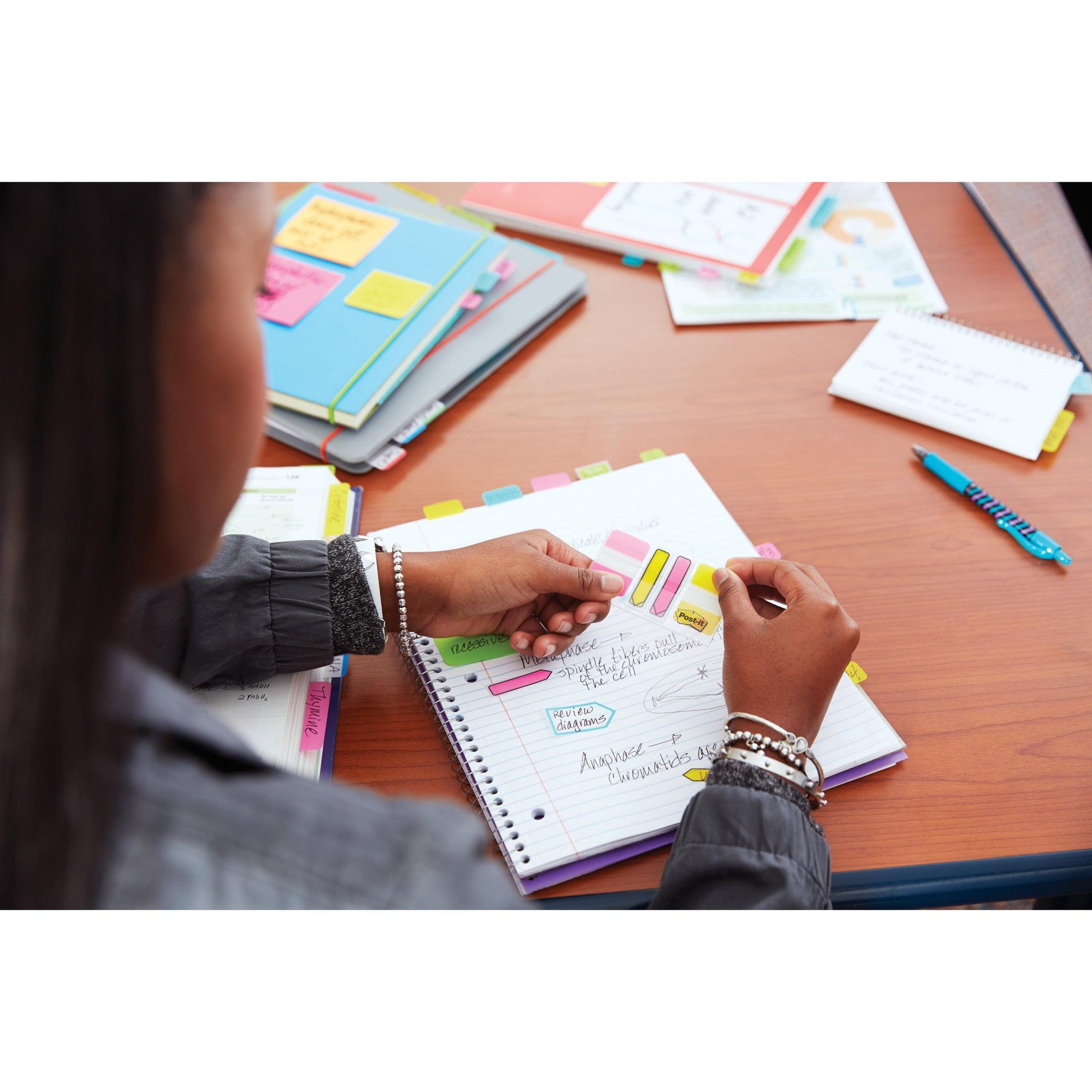 Eine Person benutzt den 3M Deutschland GmbH Post-it® Z-Notes Dispenser (PRO, Schwarz) mit Super Sticky Z-Notes (Gelb, 76x76 mm, 90 Blatt/Block) in einem Notizbuch auf einem Holztisch, umgeben von Ordnern, Papieren und einem Stift.