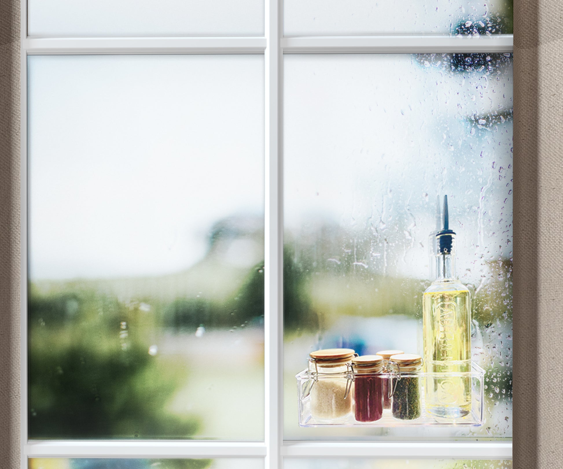 Ein Fenster mit Regentropfen zeigt eine Szene im Freien. Auf der Fensterbank stehen eine Flasche Öl, drei kleine Gläser mit goldenen Deckeln und eine Rolle Scotch-FIX™ Transparentes doppelseitiges Montageband 4910C der 3M Deutschland GmbH.