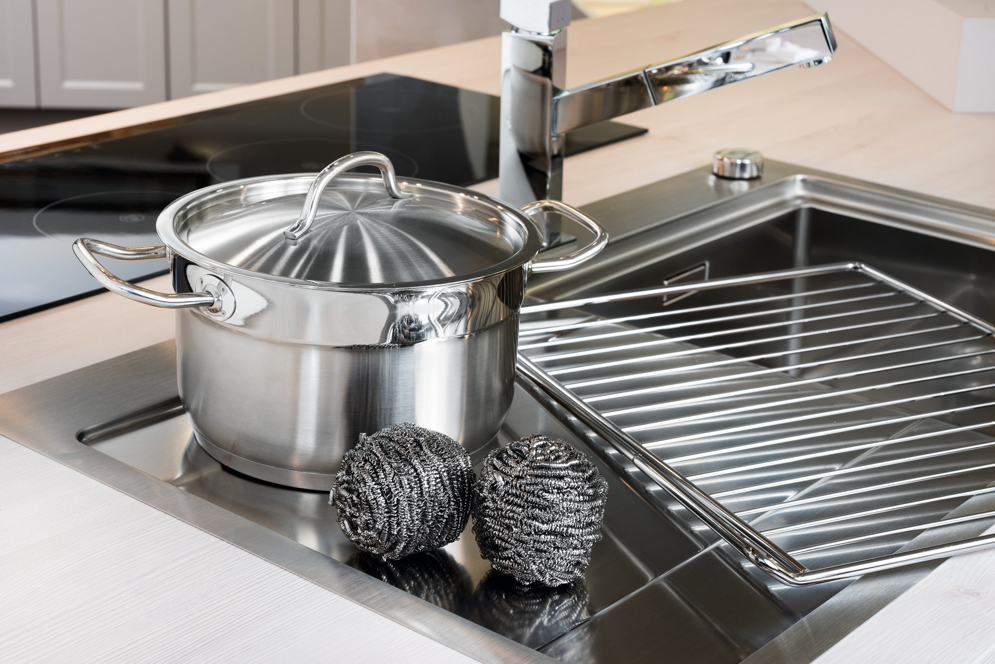 Auf der Küchentheke neben der Spüle steht ein Edelstahltopf mit Deckel neben einer Scotch-Brite® Edelstahl-Spirale der 3M Deutschland GmbH, die zu einem 3er-Pack gehört, sowie einem Metalltrockengestell und einem verchromten Wasserhahn im Hintergrund.