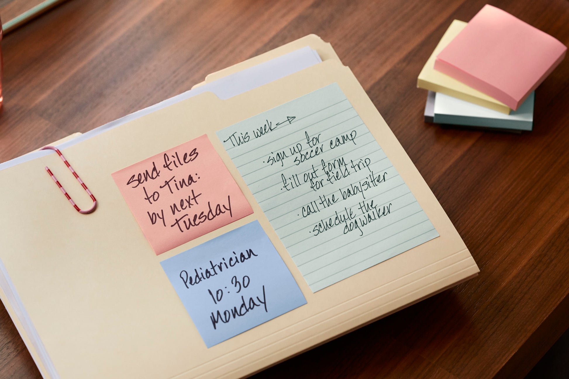 In einer Mappe auf einem Holztisch liegen drei Post-it® Recycling Notes (3M Deutschland GmbH, 38 mm x 51 mm, 100 Blatt/Block, 100% PEFC) mit Hinweisen. In der Nähe sind farbige Zettel gestapelt.