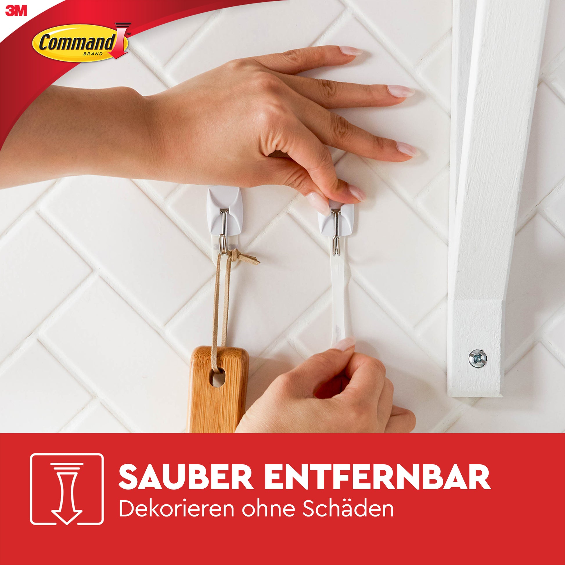 Eine Person schält einen Command™ Small Drahthaken, 17067 (1 Stück) von 3M Deutschland GmbH von einer weiß gefliesten Wand, während ein anderer Haken ein Holzutensil hält. Der deutsche Text lautet: "Sauber entfernbar. Dekorieren ohne Schäden.