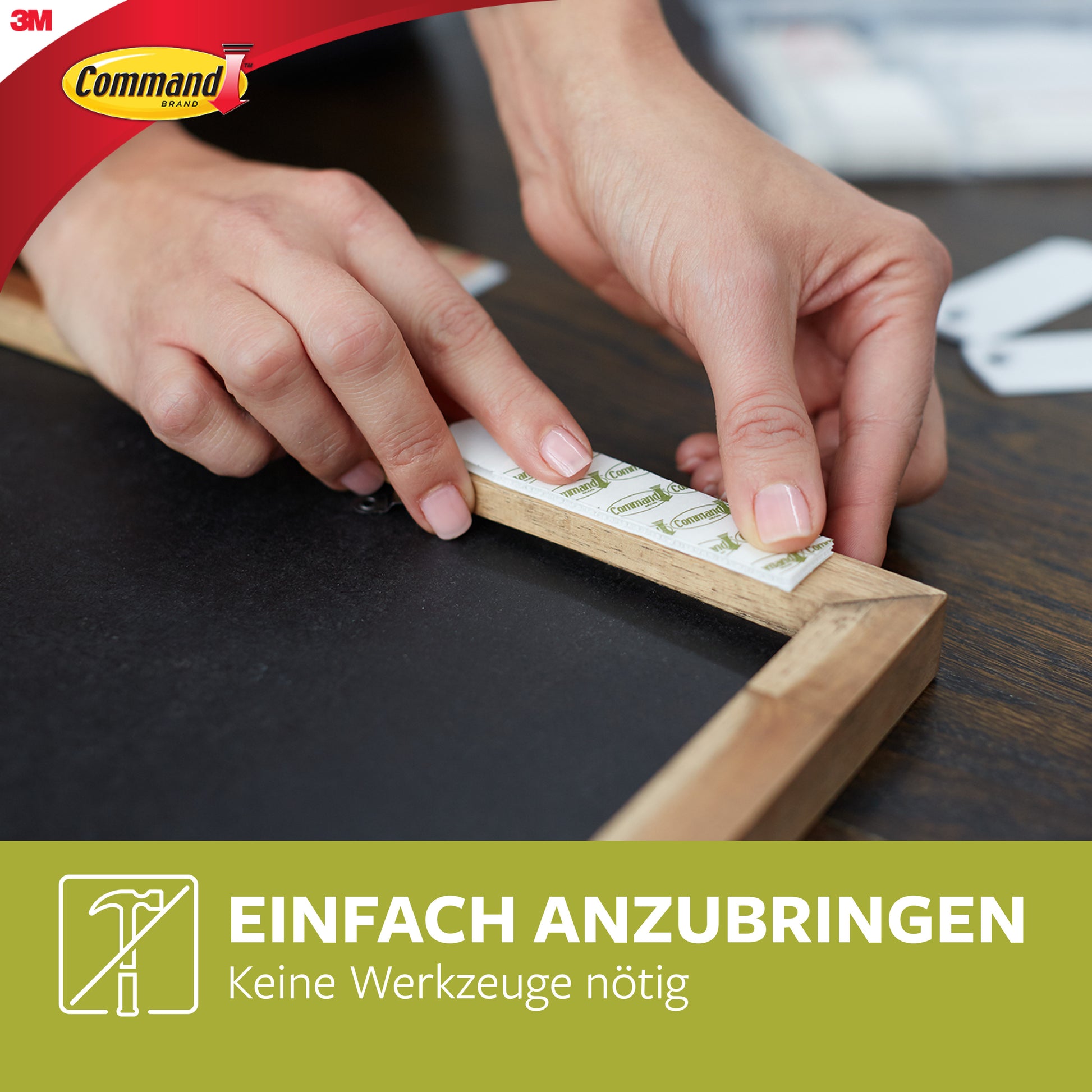 Eine Person bringt einen Holzrahmen mit Große Command™ Bilder-Montage Strips L, 12 Sets im Vorteilspack, 17206-12 von 3M Deutschland GmbH an. Das Bild zeigt das 3M Command Logo und "Einfach Anbringen, Keine Werkzeuge nötig" auf einem grünen Banner.