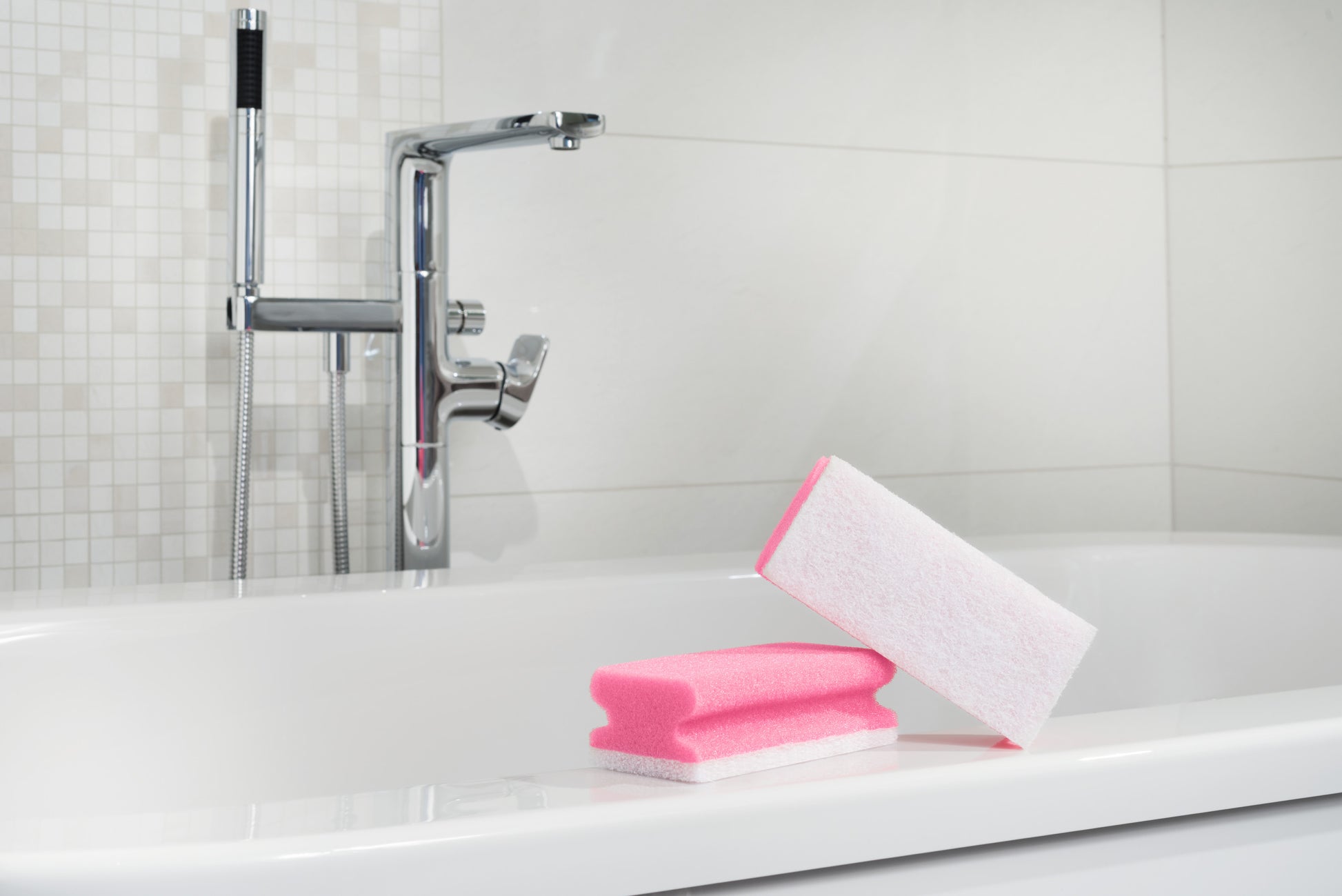 Ein Scotch-Brite® Bath Griffschwamm XXL von 3M Deutschland GmbH sitzt auf dem Rand einer weißen Badewanne mit einem verchromten Wasserhahn und einer gefliesten Wand im Hintergrund.