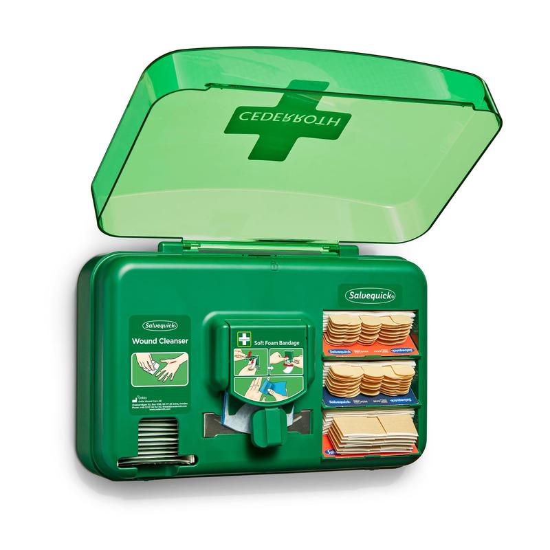 Der Orkla Wound Care AB Cederroth Wound Care Dispenser (20,3 cm x 30,6 cm x 15,5 cm, grün) wird mit geöffnetem Deckel an der Wand montiert und zeigt in den Fächern Binden, Reinigungsmittelbeutel, Klebestreifen und weiche Schaumstoffbinden; Kreuzsymbol auf dem Deckel.