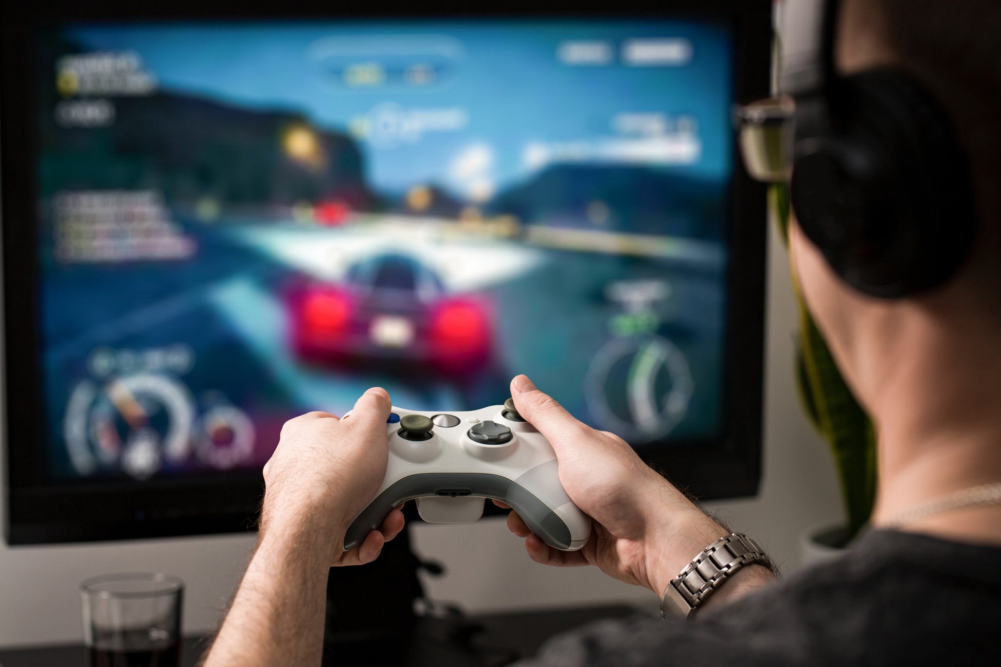 Mit Kopfhörern spielt ein Gamer ein Autorennspiel mit einem roten Sportwagen auf einem großen Monitor. In der Nähe hält das Scotch® Extremium™ INVISIBLE Hochleistungs-Klebeband (20 m x 48 mm) von 3M die Kabel geordnet und aus dem Weg.
