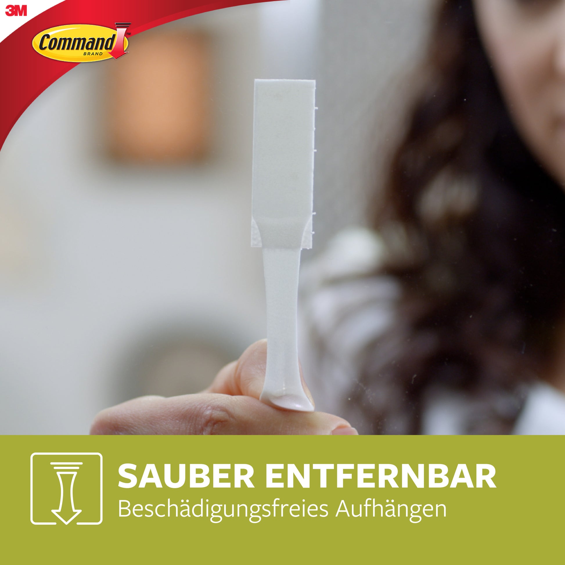 Eine Hand hält einen weißen 3M Deutschland GmbH Command™ Bilder-Montage Strip (Mittelgroß, 17201-4PK). Das Bild zeigt das Command-Logo und den deutschen Text: "Sauber entfernbar. Beschädigungsfreies Aufhängen" auf Grün.