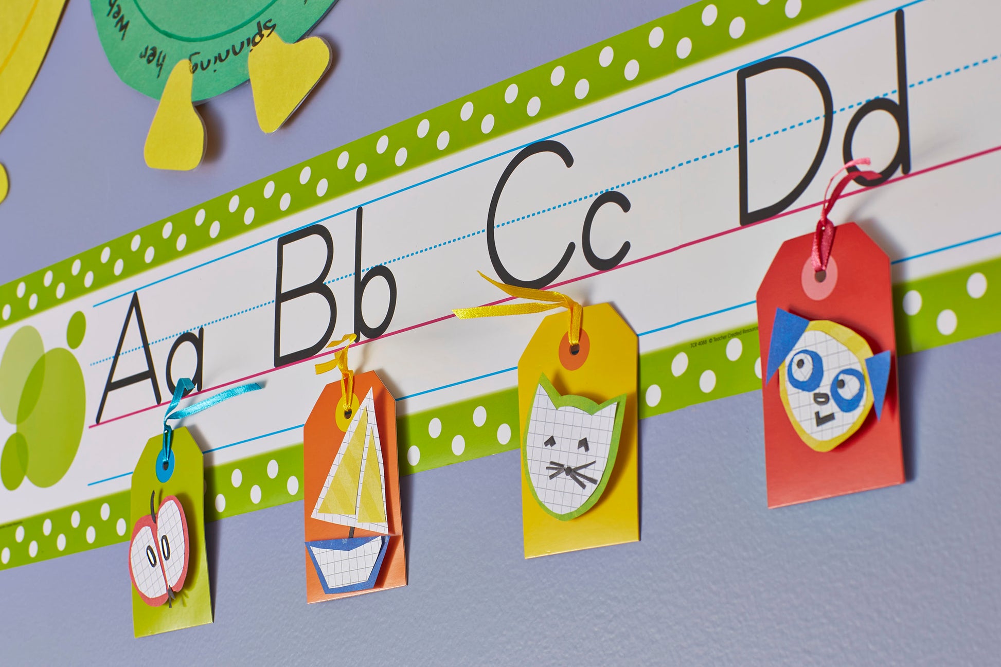 Ein Display im Klassenzimmer zeigt A, B, C und D in Groß- und Kleinbuchstaben. Vier farbige Schilder mit Zeichnungen von Schmetterlingen, Segelbooten, Katzen und Eulen werden mit 3M Scotch-FIX™ Ablösbare Klebepads (11x15 mm, 36/Packung) darunter befestigt.
