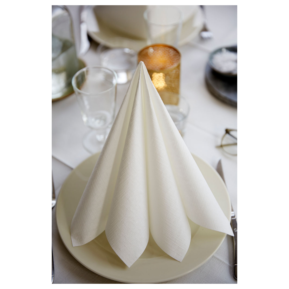 Eine sauber gefaltete Duni Dunilin®-Serviette 48 x 48 cm Weiß von Duni GmbH steht aufrecht auf einem weißen Teller inmitten von leeren Gläsern, einem runden Kerzenständer, einer Salzschale, Besteck und einer weißen Tischdecke. Das elegante Ambiente unterstreicht die stoffähnliche Textur der hochwertigen Einwegserviette.