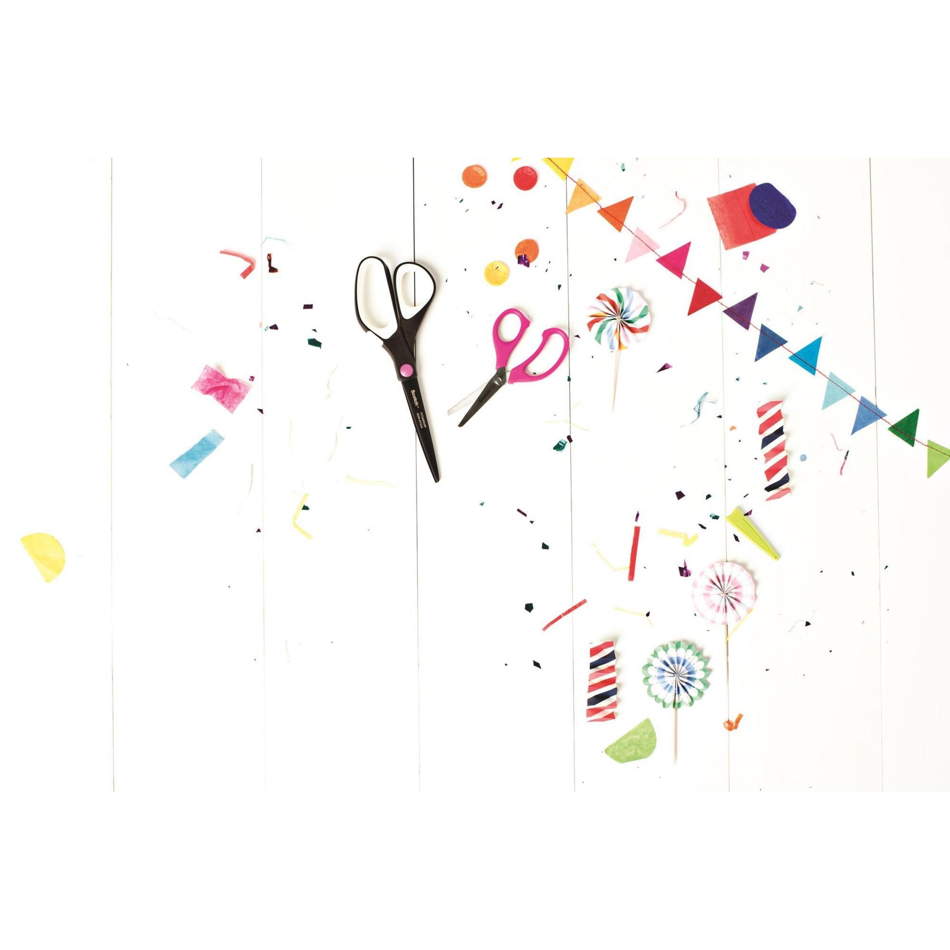 Eine Scotch™ Titanschere (20 cm) von 3M Deutschland GmbH, bunte Papierschnipsel, Konfetti, Lutscher, Kerzen und ein kleines Regenbogenbanner sind auf einer weißen Holzfläche verstreut und sorgen für eine festliche, kreative Stimmung.