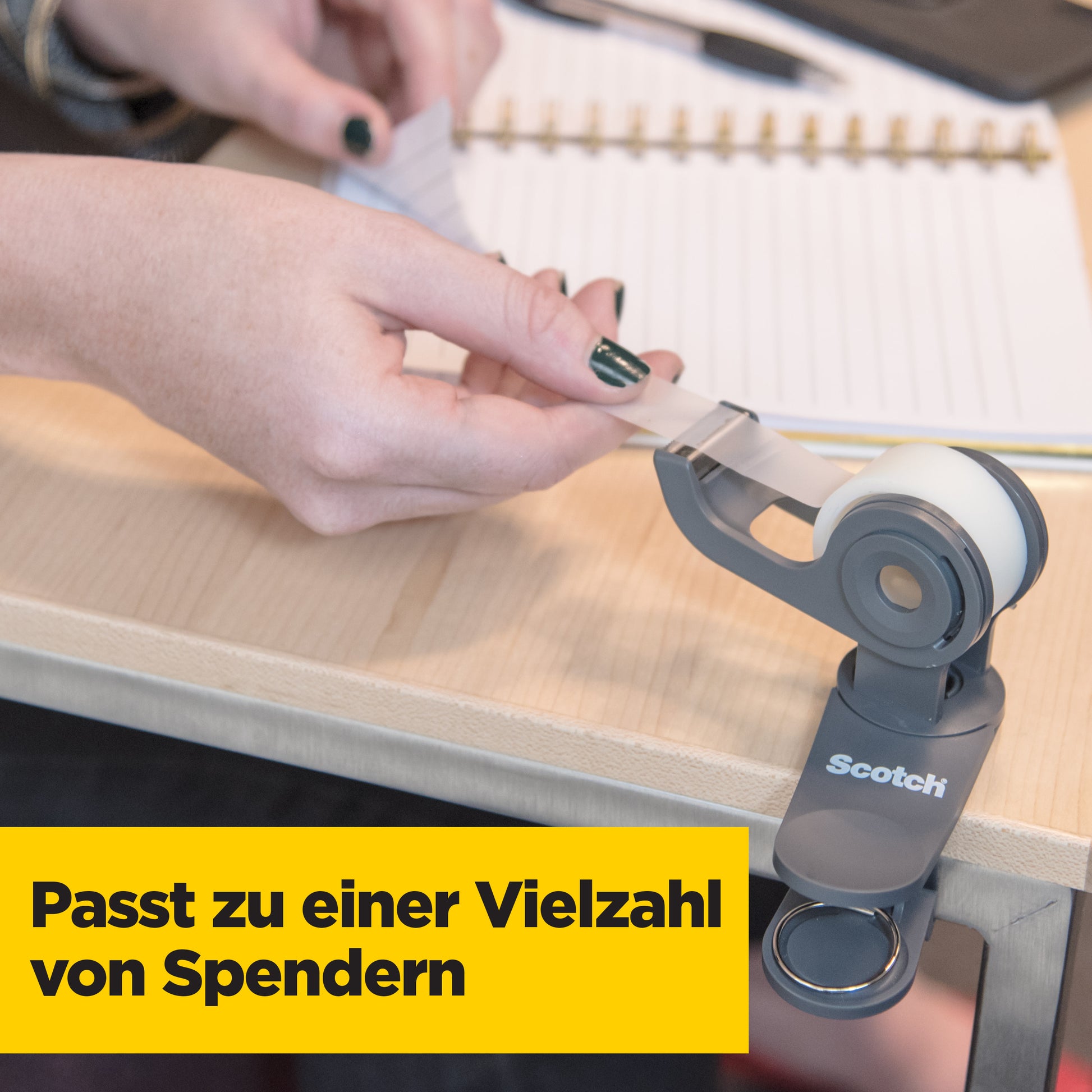 Eine Person zieht einen Streifen Scotch® Magic™ Unsichtbares Klebeband (3M Deutschland GmbH, Vorteilspack, 24 Rollen, 19 mm x 33 m) aus einem Spender auf einen Holztisch. Im Hintergrund sind ein offenes Notizbuch und ein Stift zu sehen.