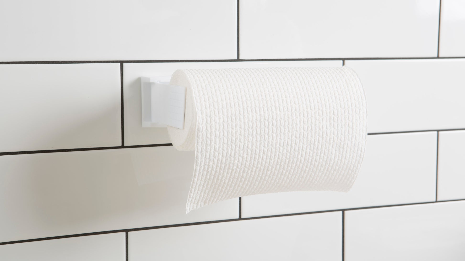 Eine Rolle weißes strukturiertes Toilettenpapier wird auf einem Halter mit 3M Deutschland GmbH Scotch-FIX™ Doppelseitige Innenmontagequadrate 4496-ST16-P, 25mm x 25mm, 16 Stück/Packung an großen weiß gefliesten Wänden mit schwarzer Fuge befestigt.