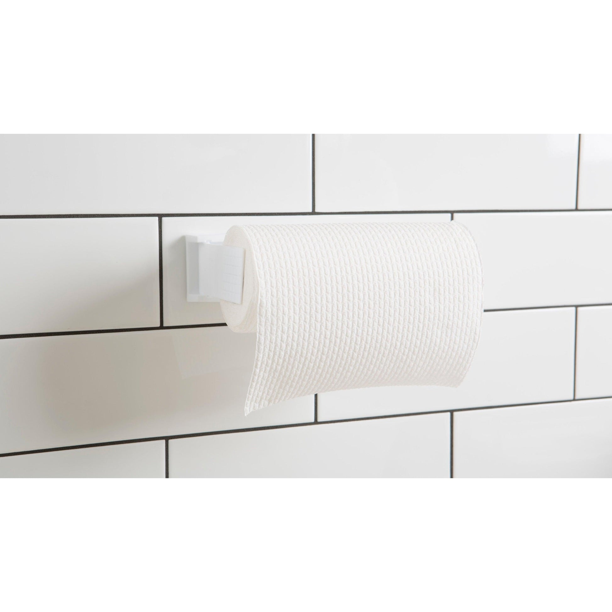 Eine Rolle weißes strukturiertes Toilettenpapier wird auf einem Halter mit 3M Deutschland GmbH Scotch-FIX™ Doppelseitige Innenmontagequadrate 4496-ST16-P, 25mm x 25mm, 16 Stück/Packung an großen weiß gefliesten Wänden mit schwarzer Fuge befestigt.