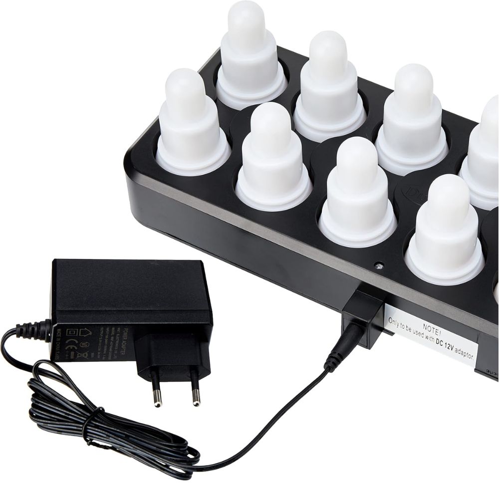 Das Produkt ist ein schwarzes rechteckiges Gerät der Duni GmbH, das zwei Reihen von sechs weißen, abgerundeten Objekten aufweist, die an Flaschenverschlüsse erinnern. Es handelt sich um das Duni 12 LED-Kerzenset mit Fernbedienung und Ladegerät, das warmweißes und mehrfarbiges Licht bietet und an ein schwarzes Netzteil angeschlossen ist.