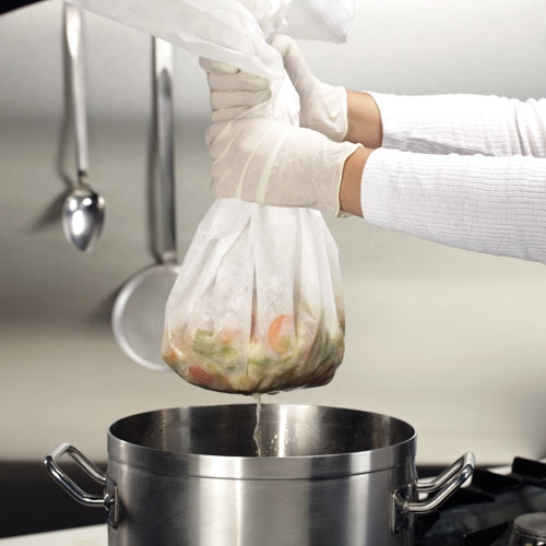 Eine Person mit weißen Handschuhen verwendet Starpak 10 Passier- und Filtertücher 100 cm x 100 cm weiss, um Gemüse effizient in einen Edelstahltopf auf dem Herd abtropfen zu lassen, während im Hintergrund Küchenutensilien an der Wand hängen.