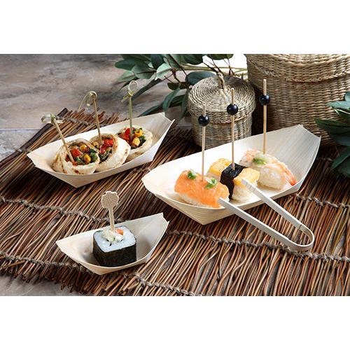 Fingerfood-Sushi und Vorspeisen werden in PAPSTAR 50 Fingerfood-Schalen, Holz „pure“ „Schiffchen“ der PAPSTAR GmbH serviert, jedes Stück auf einem dekorativen Spieß und angerichtet auf Bambus-Tischsets mit grünen Blättern und geflochtenen Körben im Hintergrund.