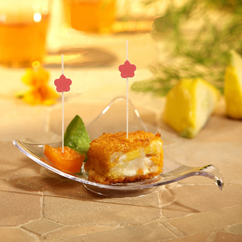 In einer kleinen Glasschale befinden sich panierte, geschichtete Lebensmittel und eine Orangenscheibe, jeweils mit einem PAPSTAR 100 Fingerfood - Picker von PAPSTAR GmbH. Neben der Orange befindet sich eine grüne Garnierung. Im Hintergrund sind unscharfe Früchte und Getränke zu sehen.