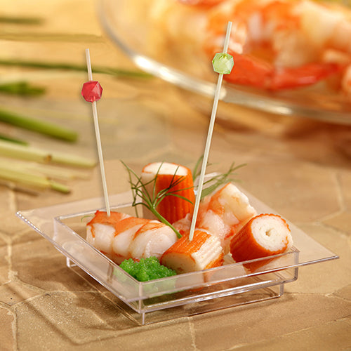 Eine kleine durchsichtige, quadratische Schale enthält Krabben- und Garnelenimitate, zwei bunte PAPSTAR 100 Fingerfood - Picker der PAPSTAR GmbH aus Bambusholz, garniert mit grünen Kräutern und einer kleinen Portion grünem Rogen.