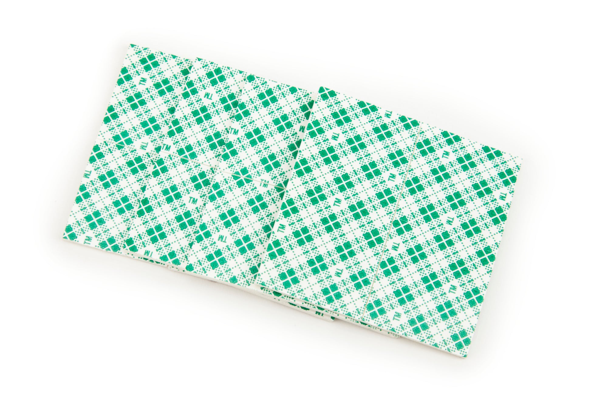 Zwei Scotch-FIX™ Doppelseitige Innenmontagequadrate (25mm x 25mm) von 3M Deutschland GmbH liegen nebeneinander und zeigen ihre grün und weiß gemusterte Rückseite.