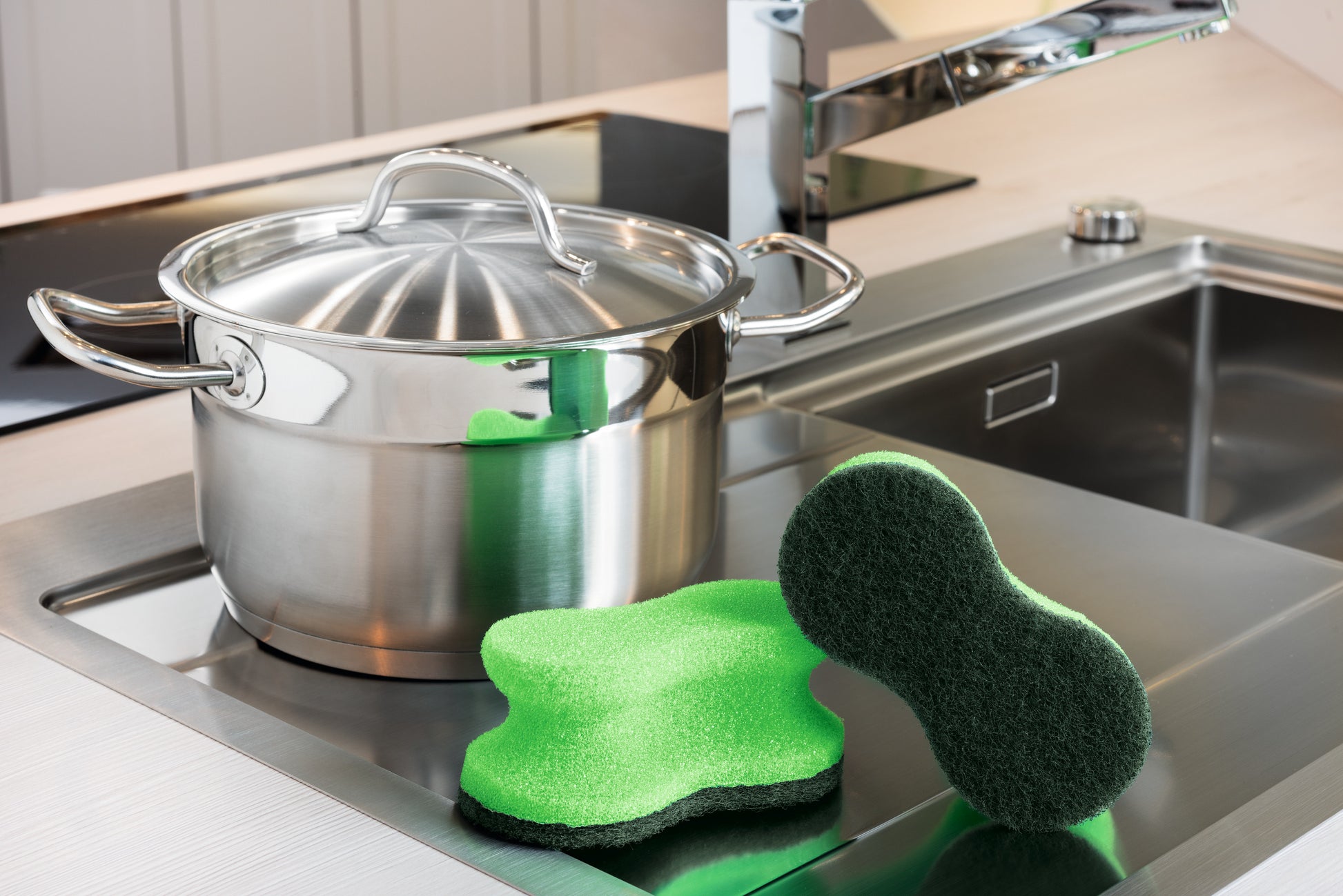 Ein Edelstahltopf mit Deckel steht auf der Küchentheke neben der Spüle. Zwei Scotch-Brite® Classic Reinigungsschwämme der 3M Deutschland GmbH sind im Vordergrund neben dem Topf platziert.