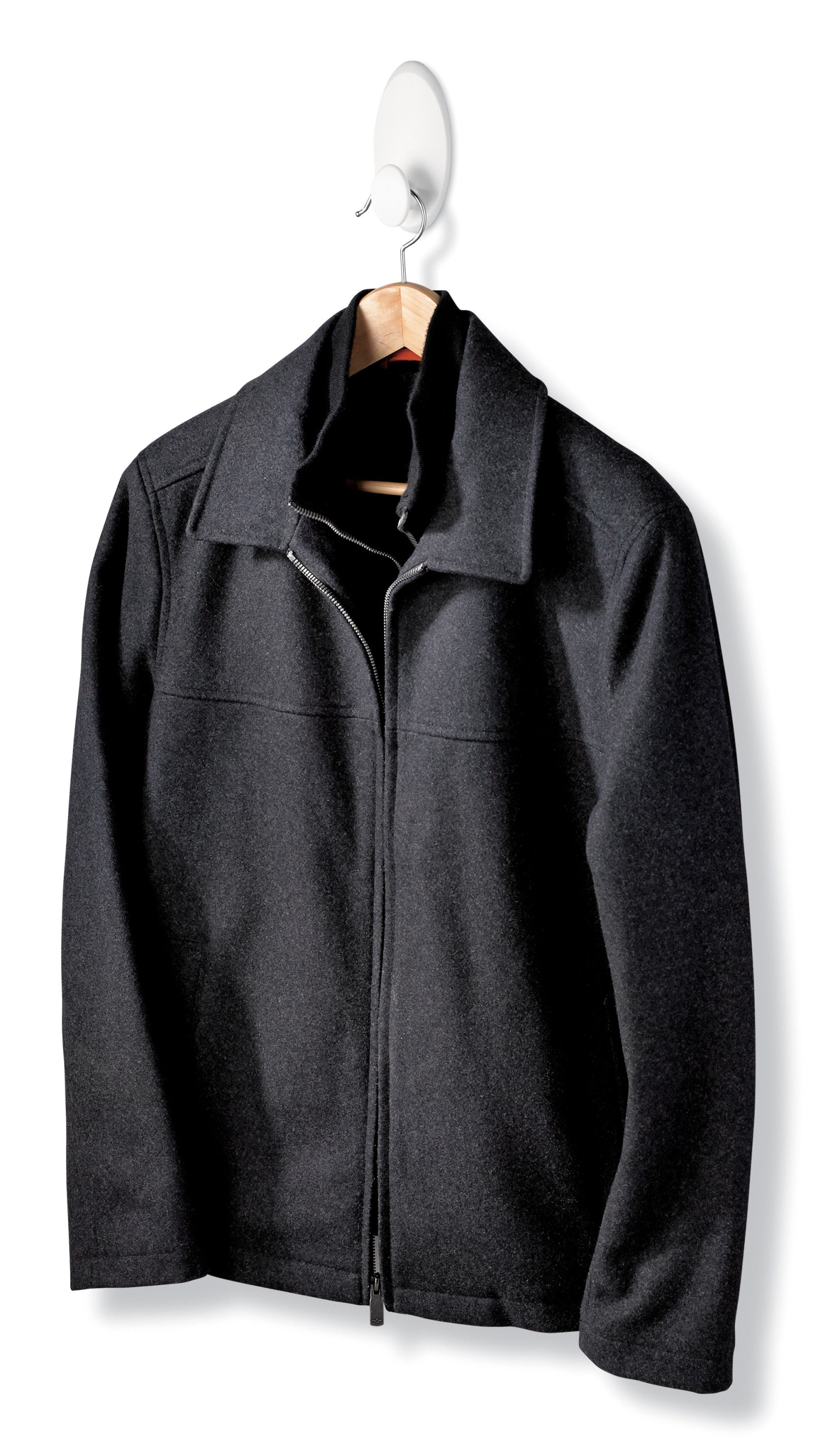 Eine schwarze Jacke mit Reißverschluss und Kragen hängt an einem Holzbügel, der auf einem Command™ Kleider-Haken, 17019-FGN (1 Stück) von 3M Deutschland GmbH vor weißem Hintergrund angebracht ist.