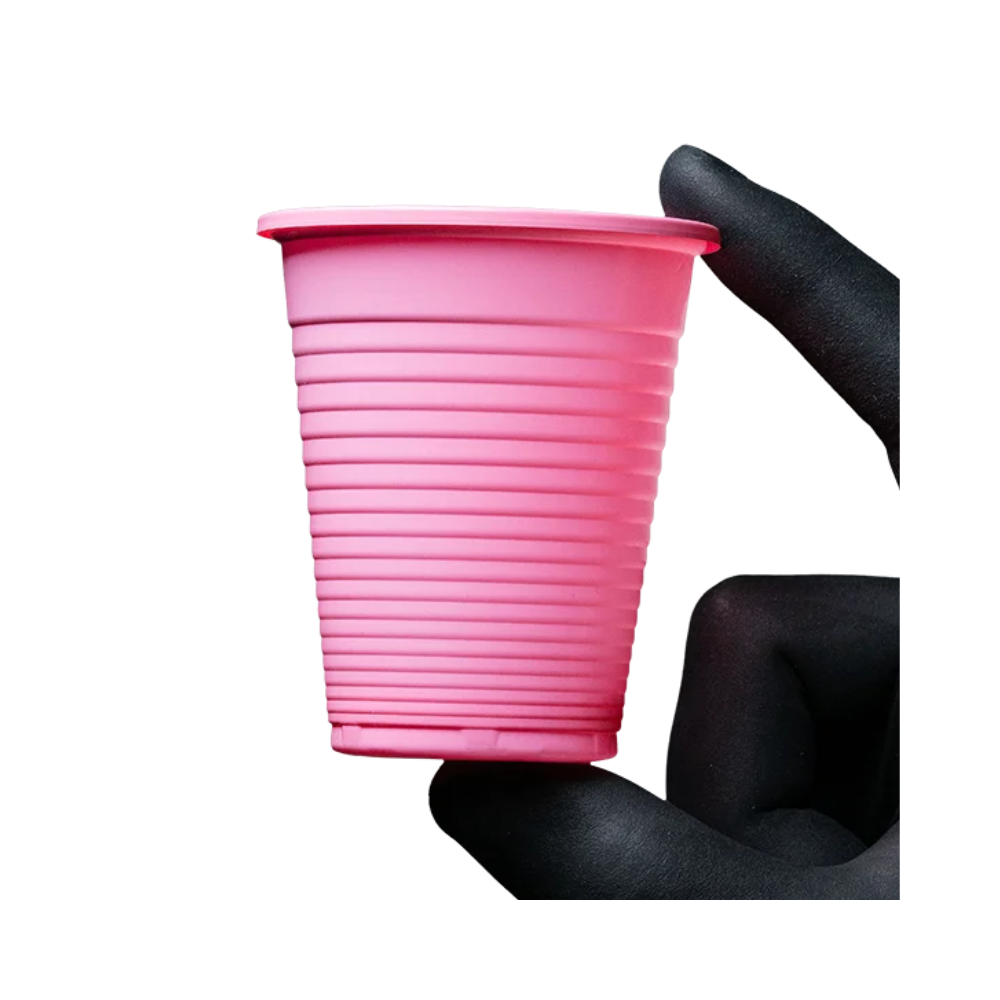 Eine elegant behandschuhte Hand in Schwarz hält zart einen kleinen, rosa, gerippten AMPri Dental PP-Mundspülbecher der AMPri Handelsgesellschaft mbH vor einem makellos weißen Hintergrund.