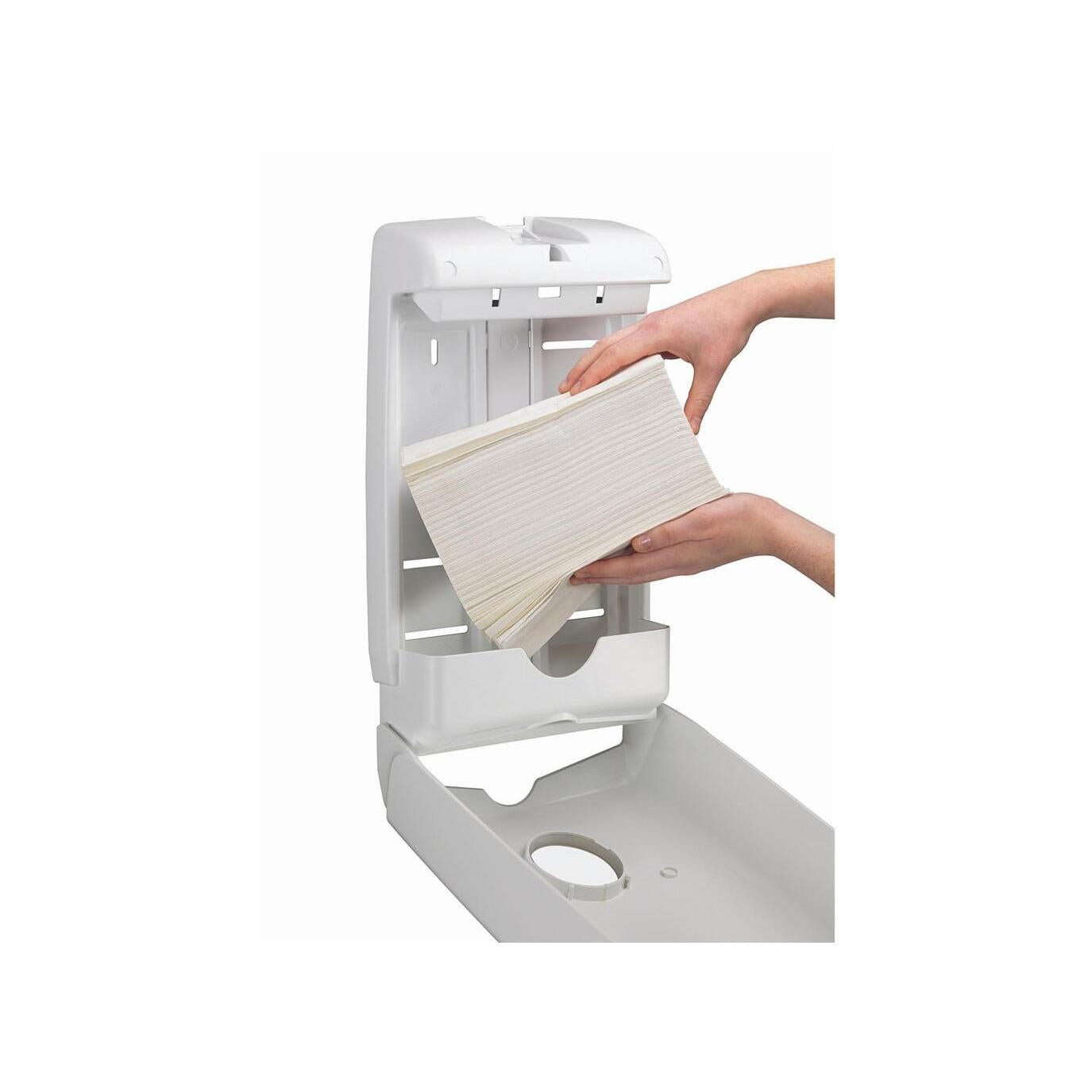 Jemand füllt den an der Wand montierten Aquarius™ Slimfold™ Spender für gefaltete Handtücher (Weiß) von Kimberly-Clark GmbH nach, indem er den Deckel anhebt und einen Stapel gefalteter Handtücher in diesen platzsparenden Spender einlegt.
