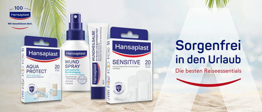 Hansaplast Werbeanzeige mit vier Produkten auf einem sandigen Strandhintergrund unter Palmen: Aqua Protect Pflaster (20 Stück), Wundspray zur antiseptischen Wundreinigung, Wundheilsalbe und Sensitive Pflaster (20 Stück). Rechts der Slogan: ‚Sorgenfrei in den Urlaub – Die besten Reiseessentials‘.