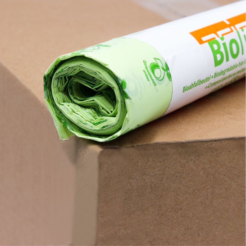 Eine Rolle hellgrüner DEISS Biomüllbeutel 30 Liter, 06030, die zu 100% kompostierbar sind, liegt auf einem braunen Karton. Die Verpackung ist teilweise sichtbar und zeigt ein umweltfreundliches Logo und den Schriftzug „Bio“ in fetten orangefarbenen Buchstaben der EMIL DEISS KG (GmbH + Co.).